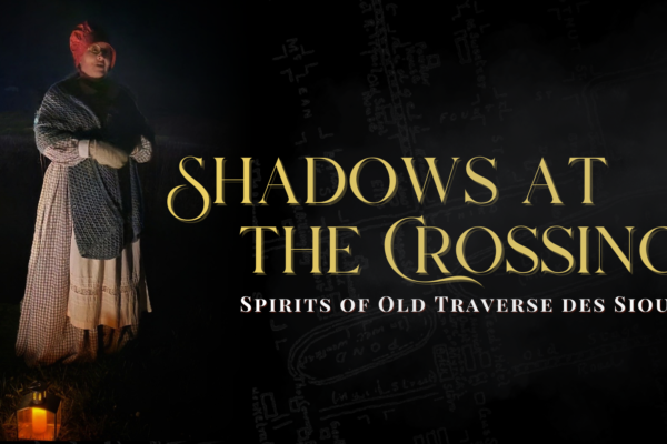 A person dressed in historical attire stands in the dark holding a lantern, beside text that reads, "Shadows at the Crossing: Spirits of Old Traverse des Sioux." A faint map is visible in the background.